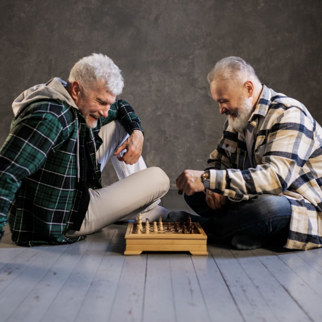 dos hombres mayores sentados en el suelo jugando ajedrez